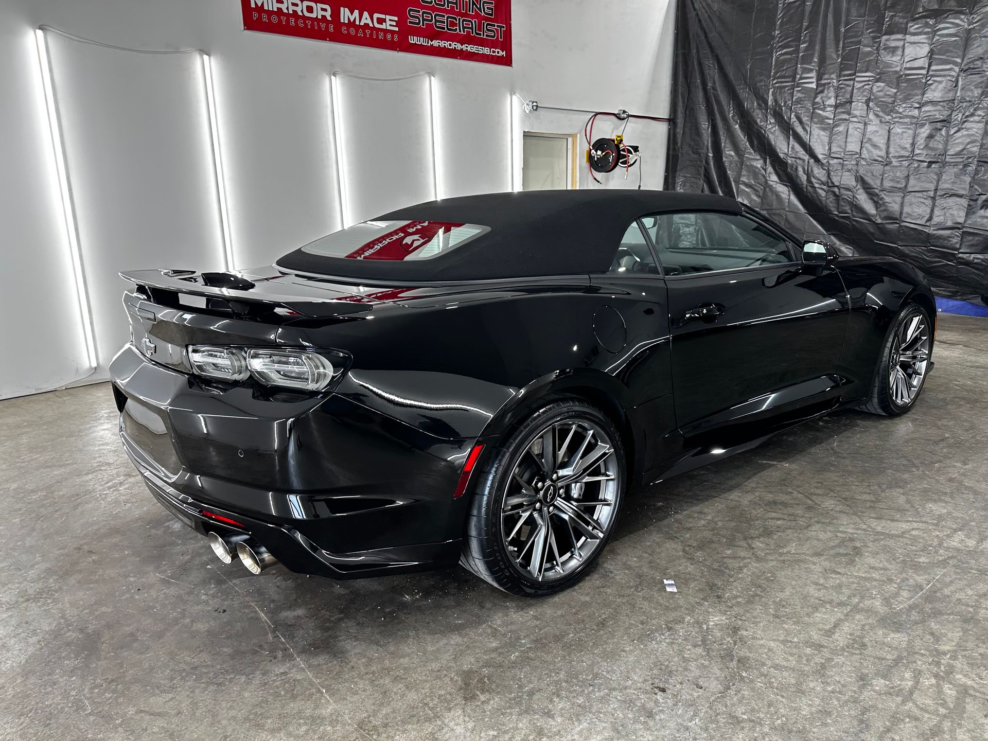A black Chevrolet Camaro convertible parked at a slight angle in a clean, brightly lit indoor detailing shop.