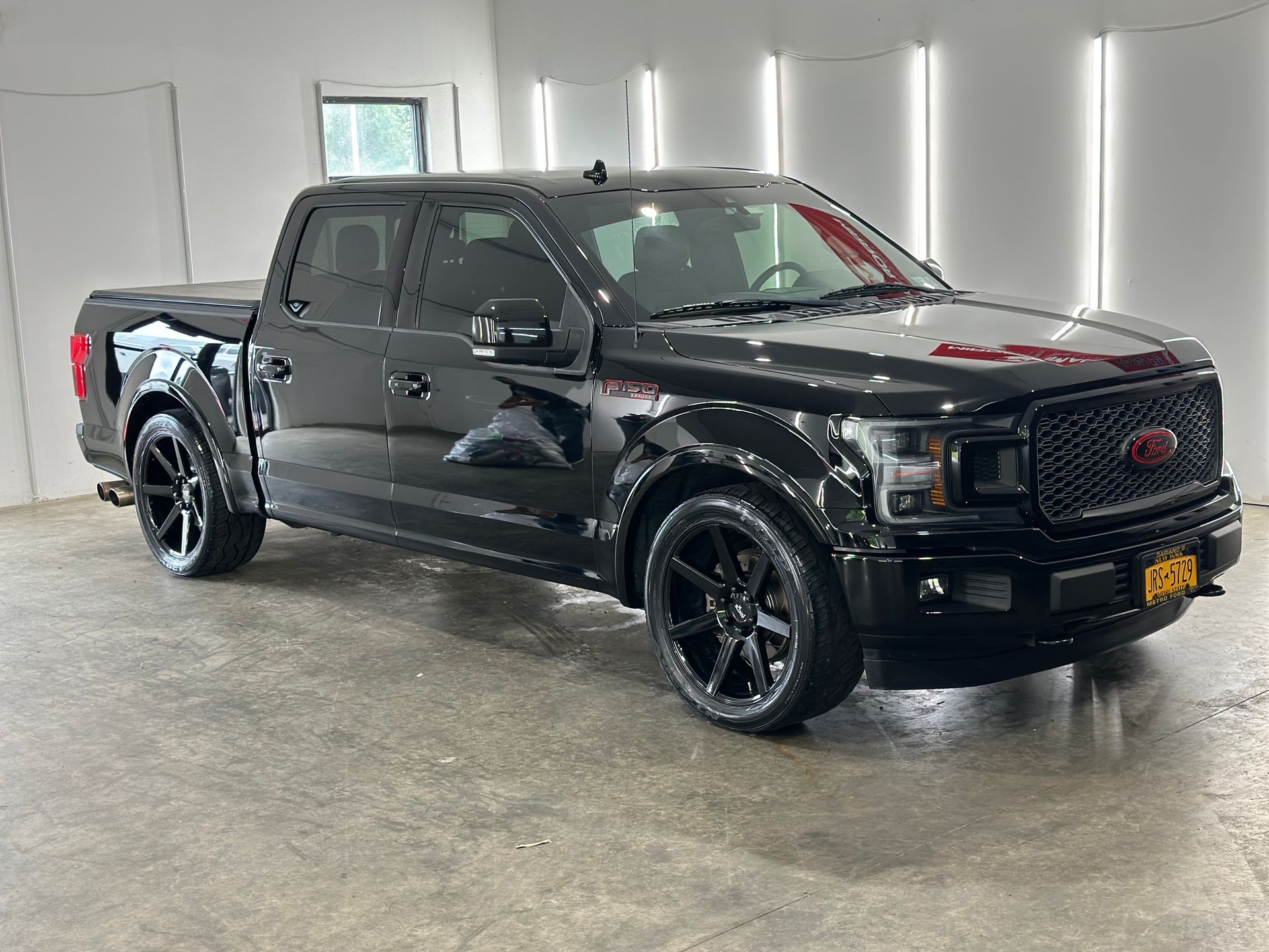 A black Ford F-150 crew cab pickup truck with black wheels parked inside a brightly lit garage.
