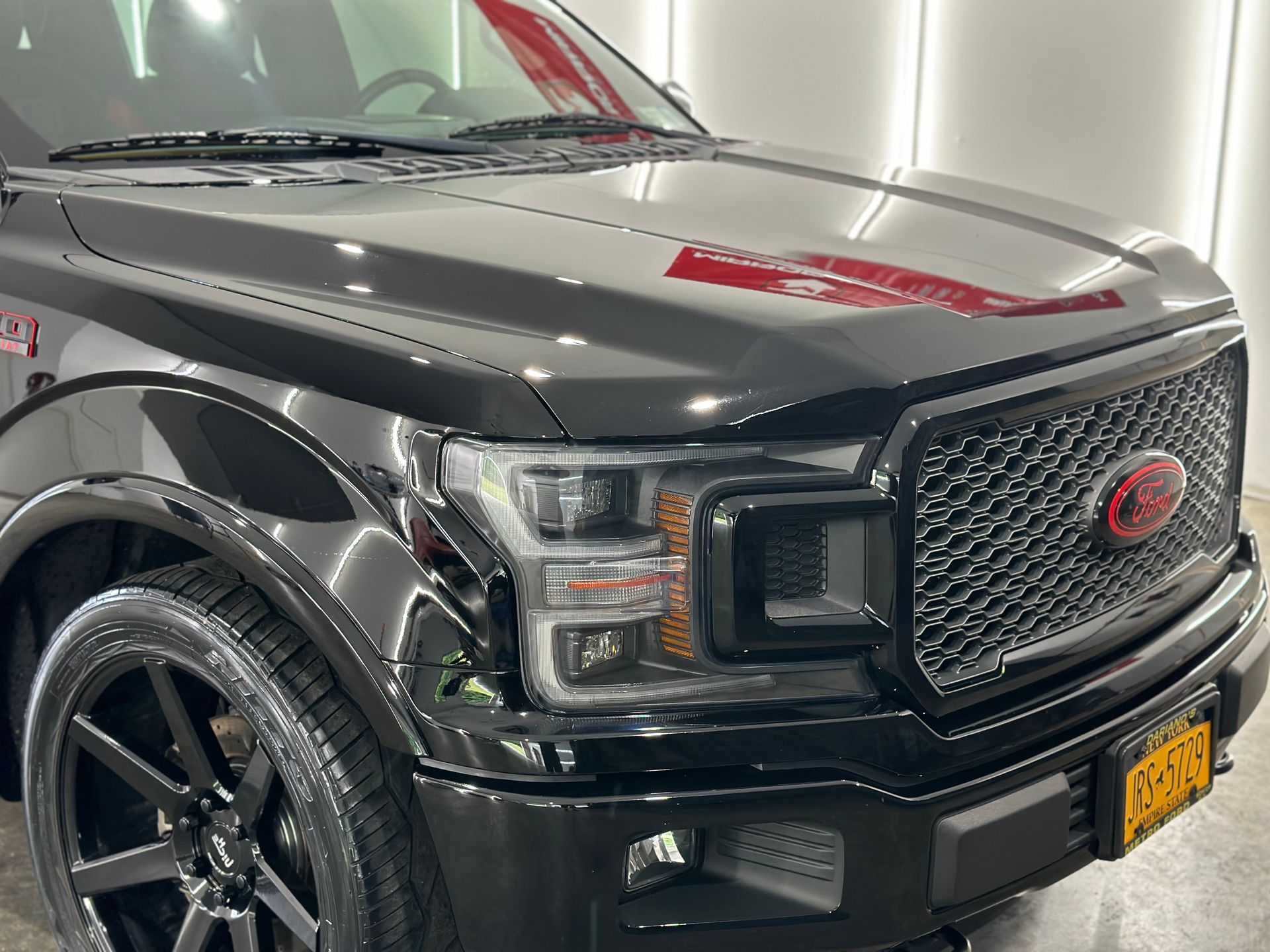A close-up of the front quarter of a shiny black Ford F-150 truck with custom wheels, a black grille, and a red emblem.