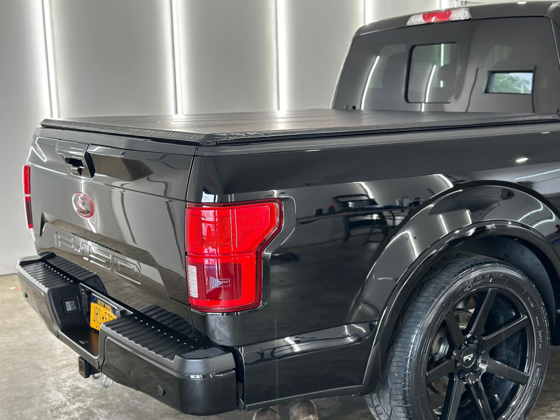 Rear view of a black Ford F-150 pickup truck with a bed cover, parked in an indoor garage.