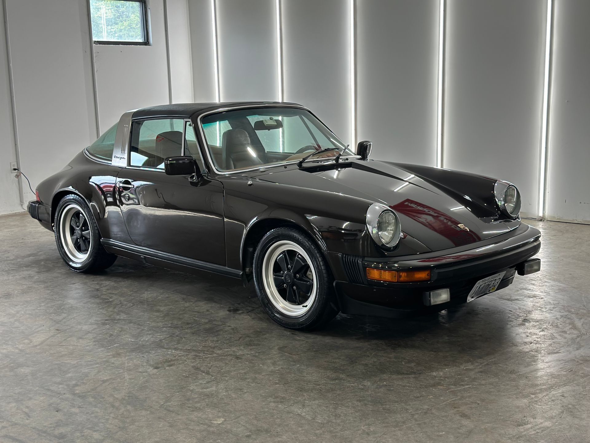 A dark brown vintage Porsche 911 Targa parked in a bright, modern garage with vertical lights.