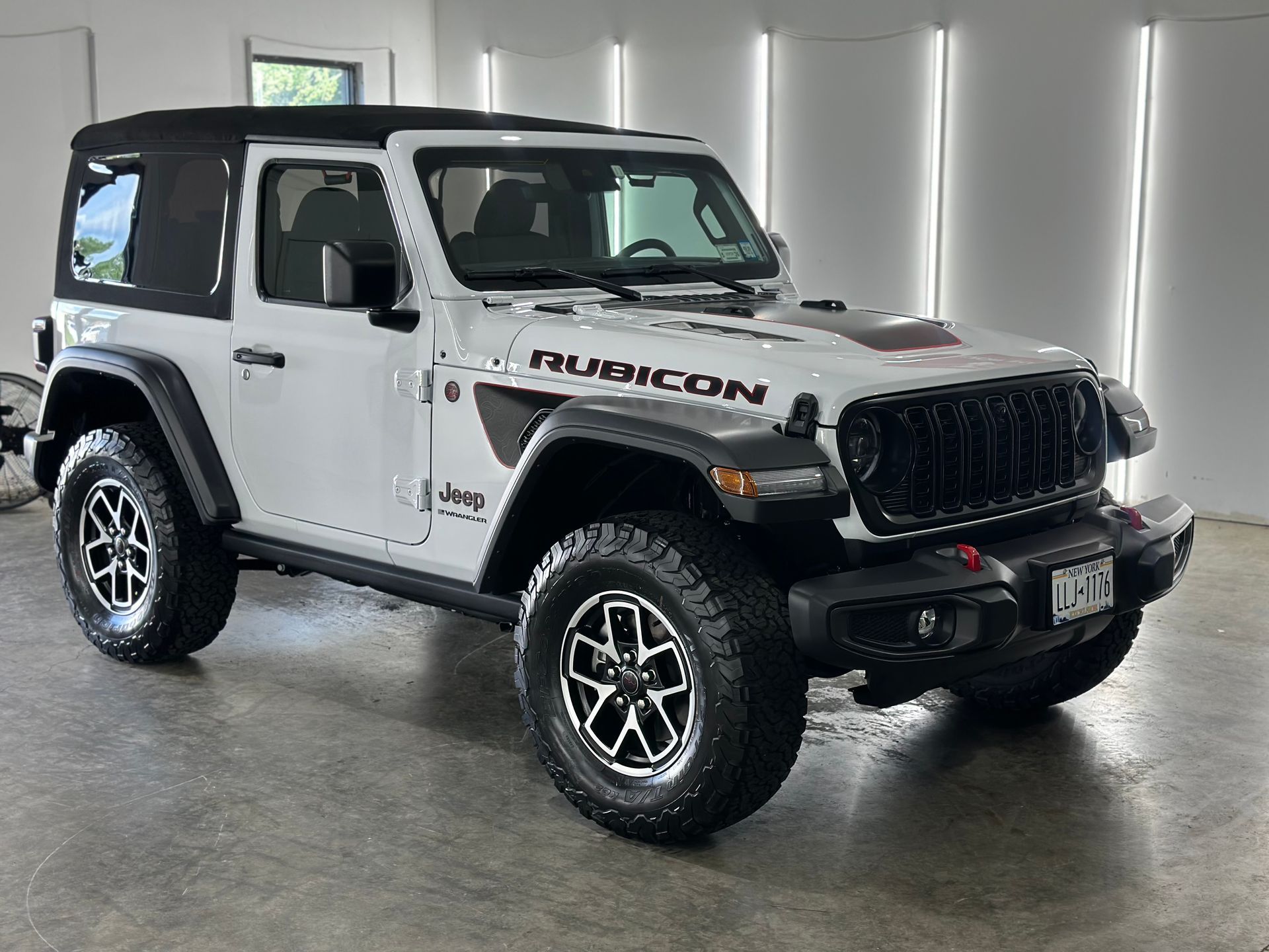 A white Jeep Wrangler Rubicon two-door SUV parked inside a garage with vertical LED wall lights.