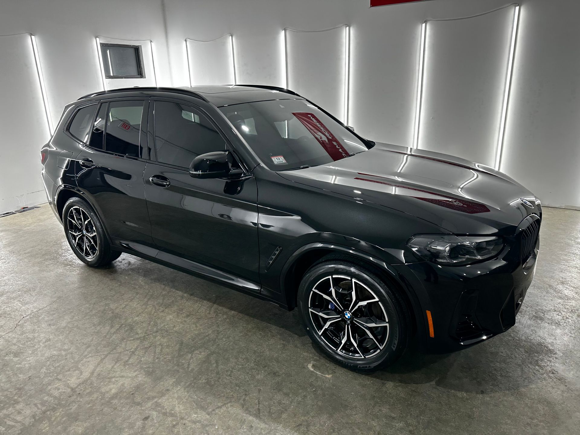 A black BMW SUV parked in a well-lit showroom with overhead vertical lighting.