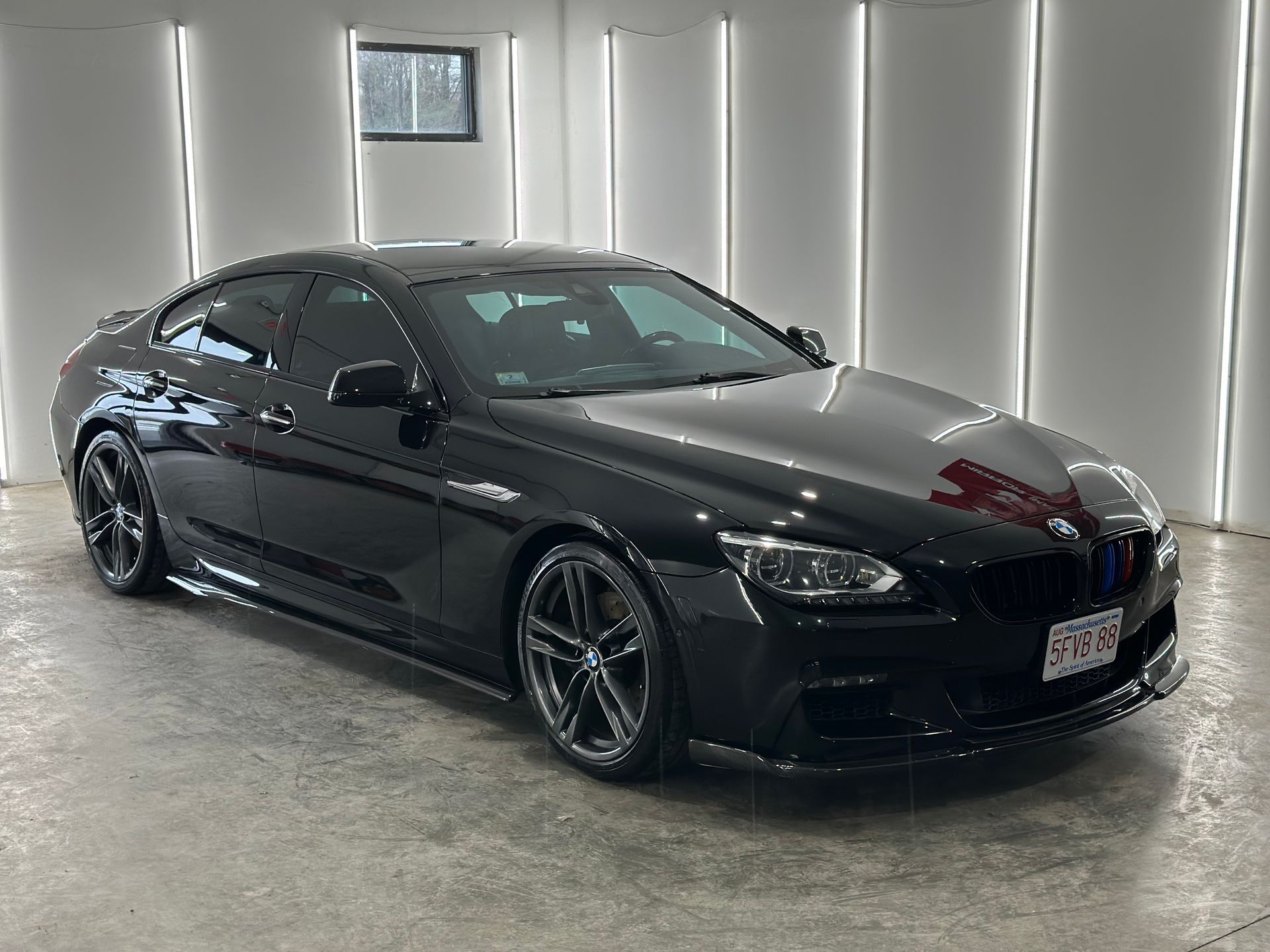 A black BMW 6 Series Gran Coupe parked in a brightly lit, modern garage with white walls and vertical light strips.