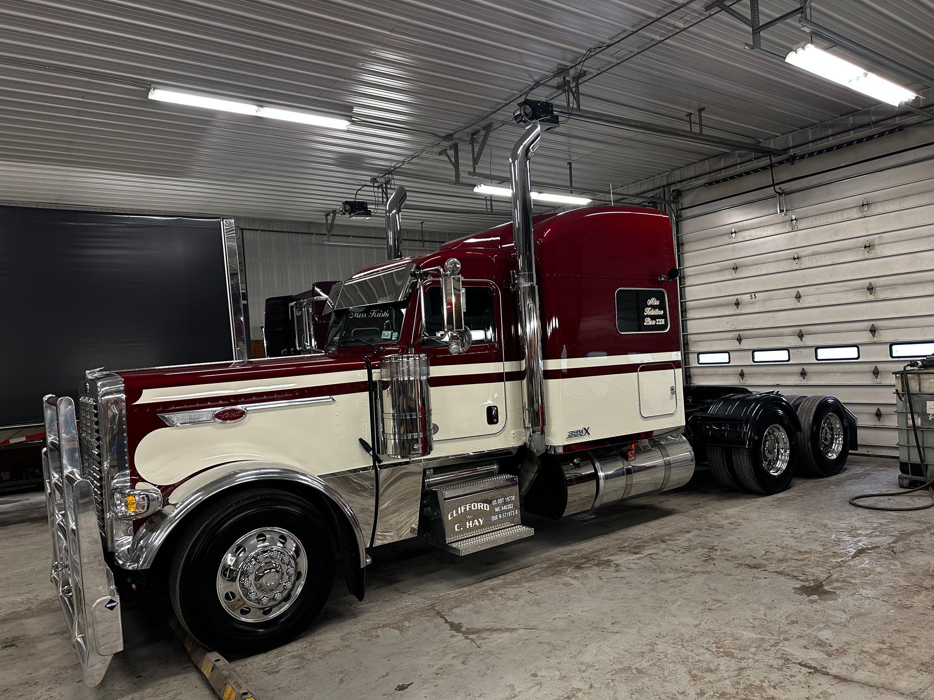 A cherry-red and cream-colored semi-truck with shiny chrome details parked inside a garage.