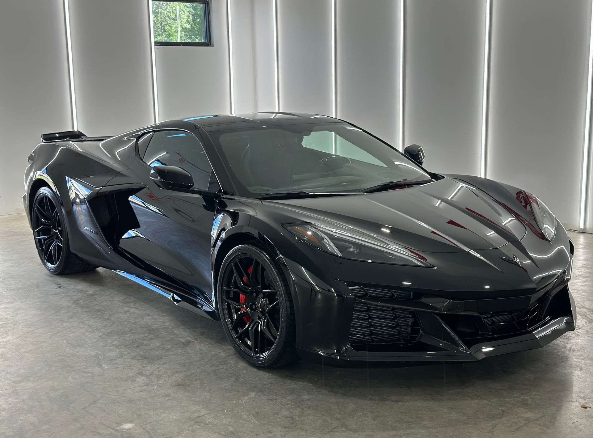 A sleek, black Chevrolet Corvette C8 E-Ray parked in a brightly lit studio with vertical LED light panels.