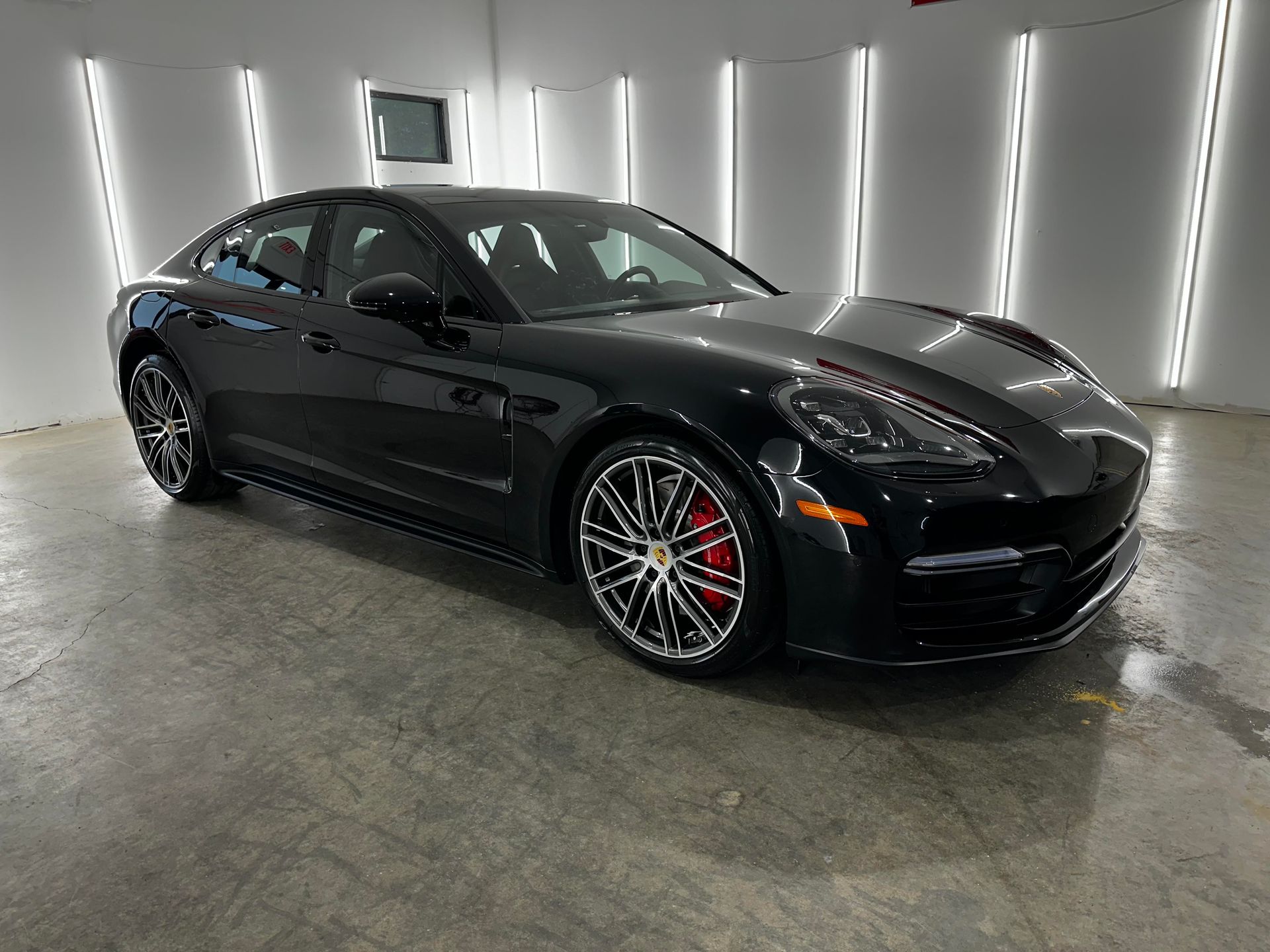 A sleek black Porsche Panamera parked in a bright, modern studio with vertical wall lights.