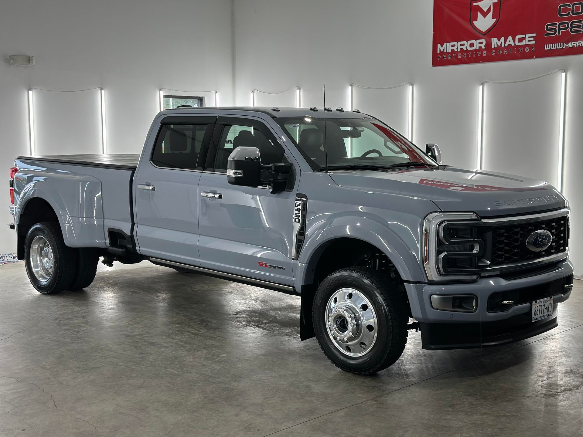 A gray Ford F-series dually pickup truck parked in a well-lit auto shop with a Mirror Image logo on the wall.