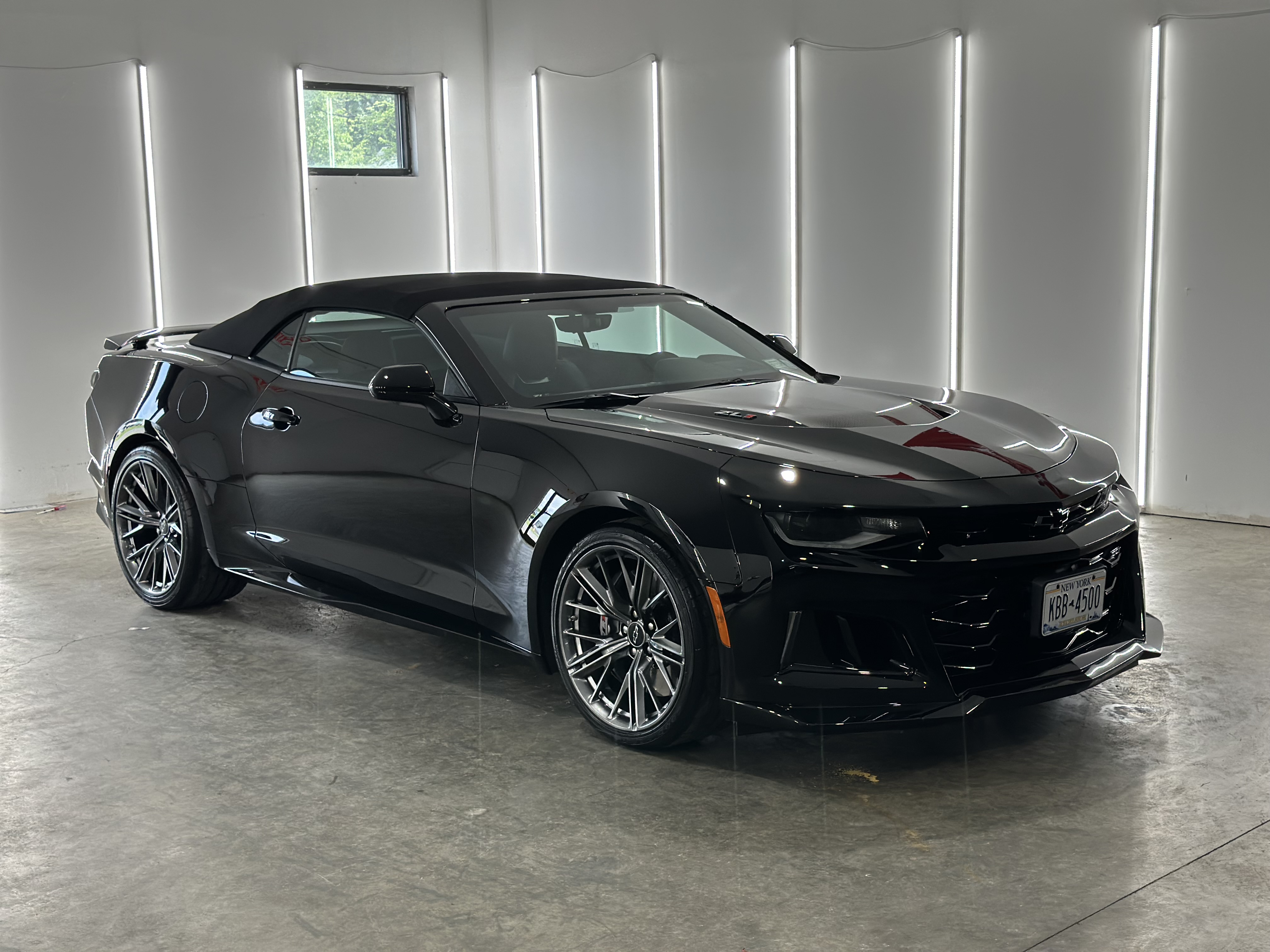 A black Chevrolet Camaro convertible parked in a bright, modern studio with white walls and vertical light strips.