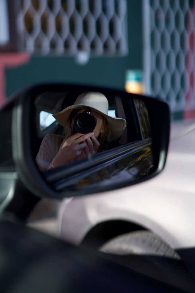a woman in a hat is taking a picture in the rear view mirror of a car