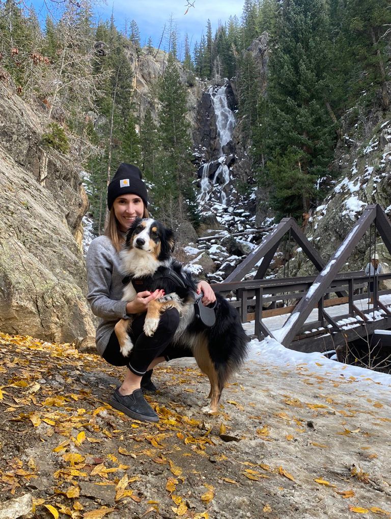 a woman kneeling down with a dog in front of a waterfall