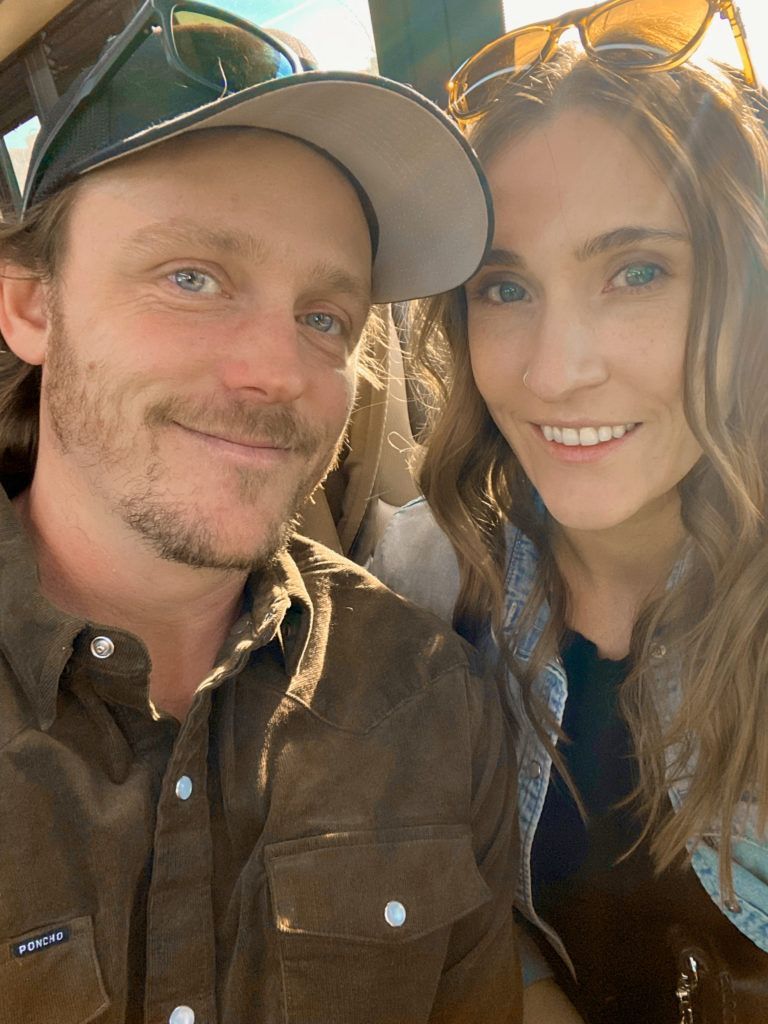 a man wearing a poncho shirt smiles next to a woman