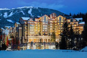 a large building with a mountain in the background is surrounded by snow and trees .