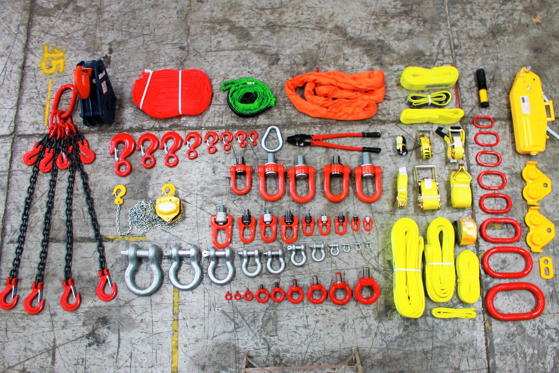 Equipos de aparejo variados, incluidas cadenas, ganchos, grilletes y eslingas, dispuestos sobre una superficie gris.