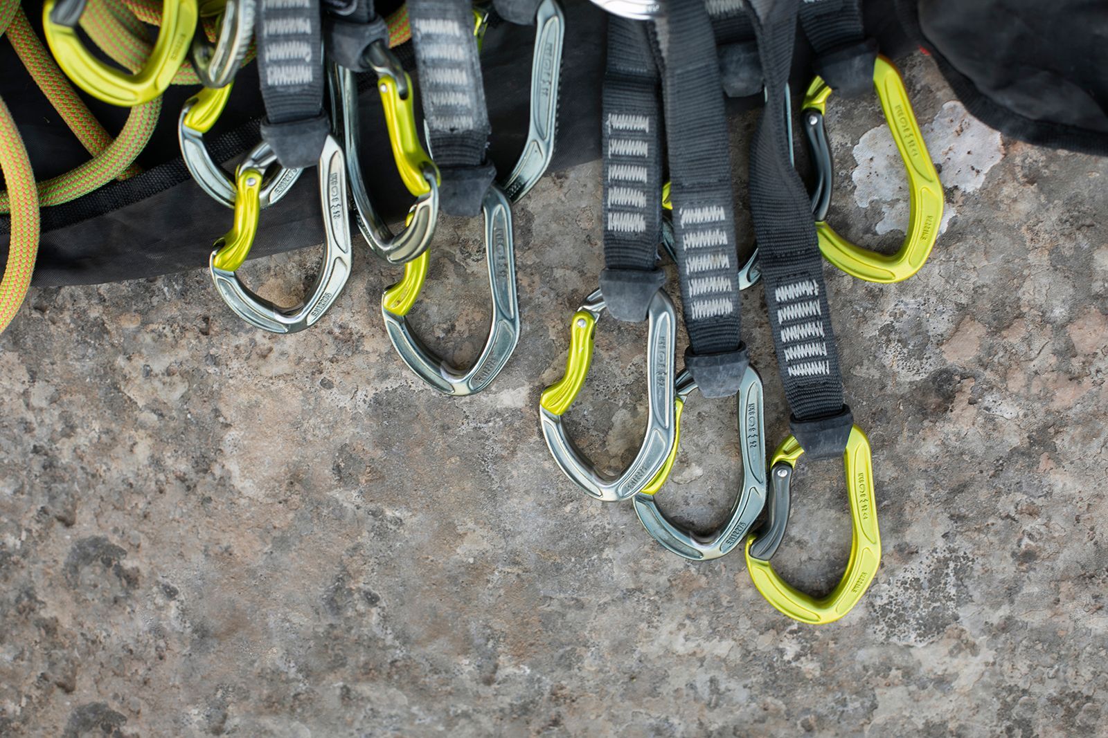 Equipo de escalada: mosquetones amarillos y plateados sobre eslingas negras, apoyados sobre una superficie de hormigón.