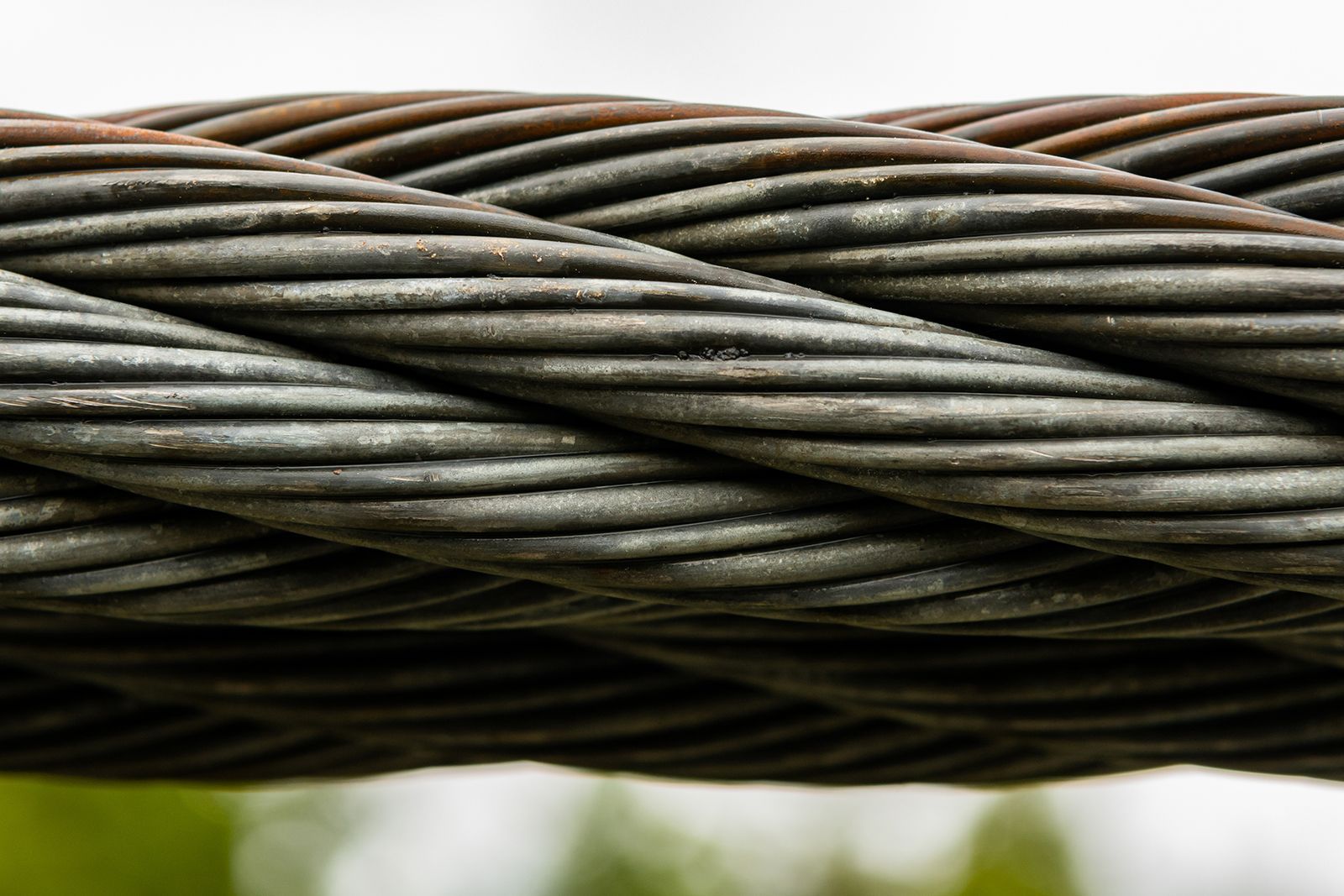 Primer plano de un cable metálico grueso y trenzado, de color gris oscuro, con hebras retorcidas visibles.
