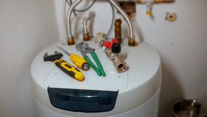 Tools on top of a water heater, including a wrench, screwdriver, pliers, and valve.
