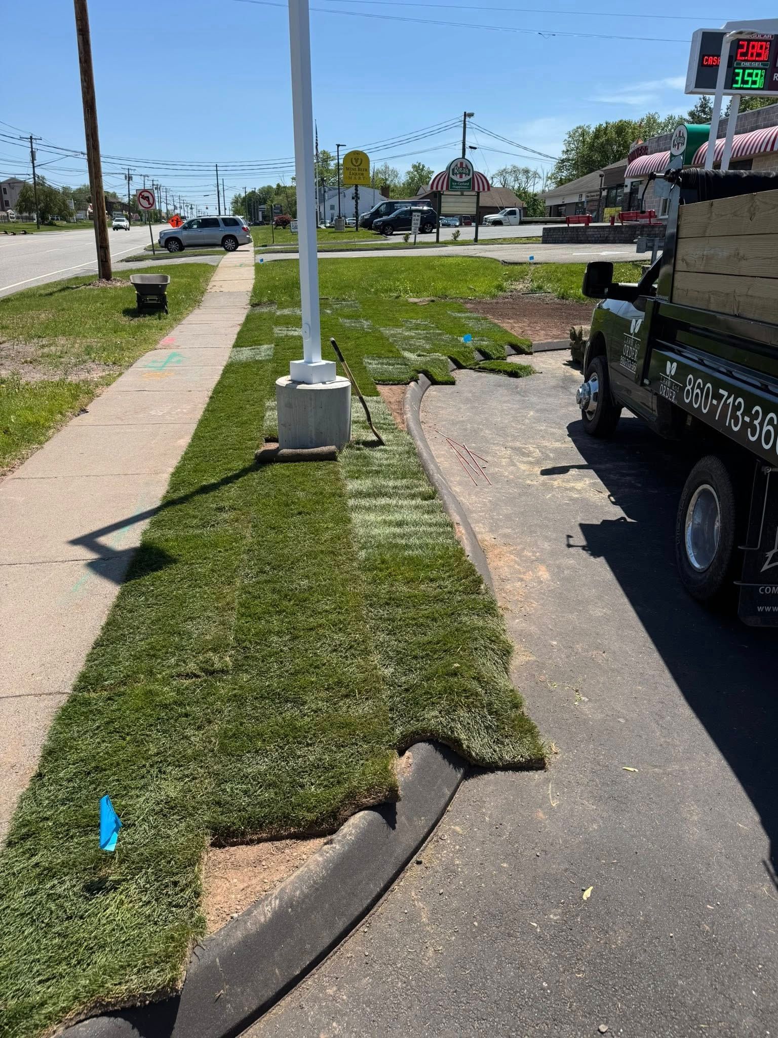 Sidewalk beside a grassy median and parked utility truck at a street intersection, with a crosswalk signal ahead.