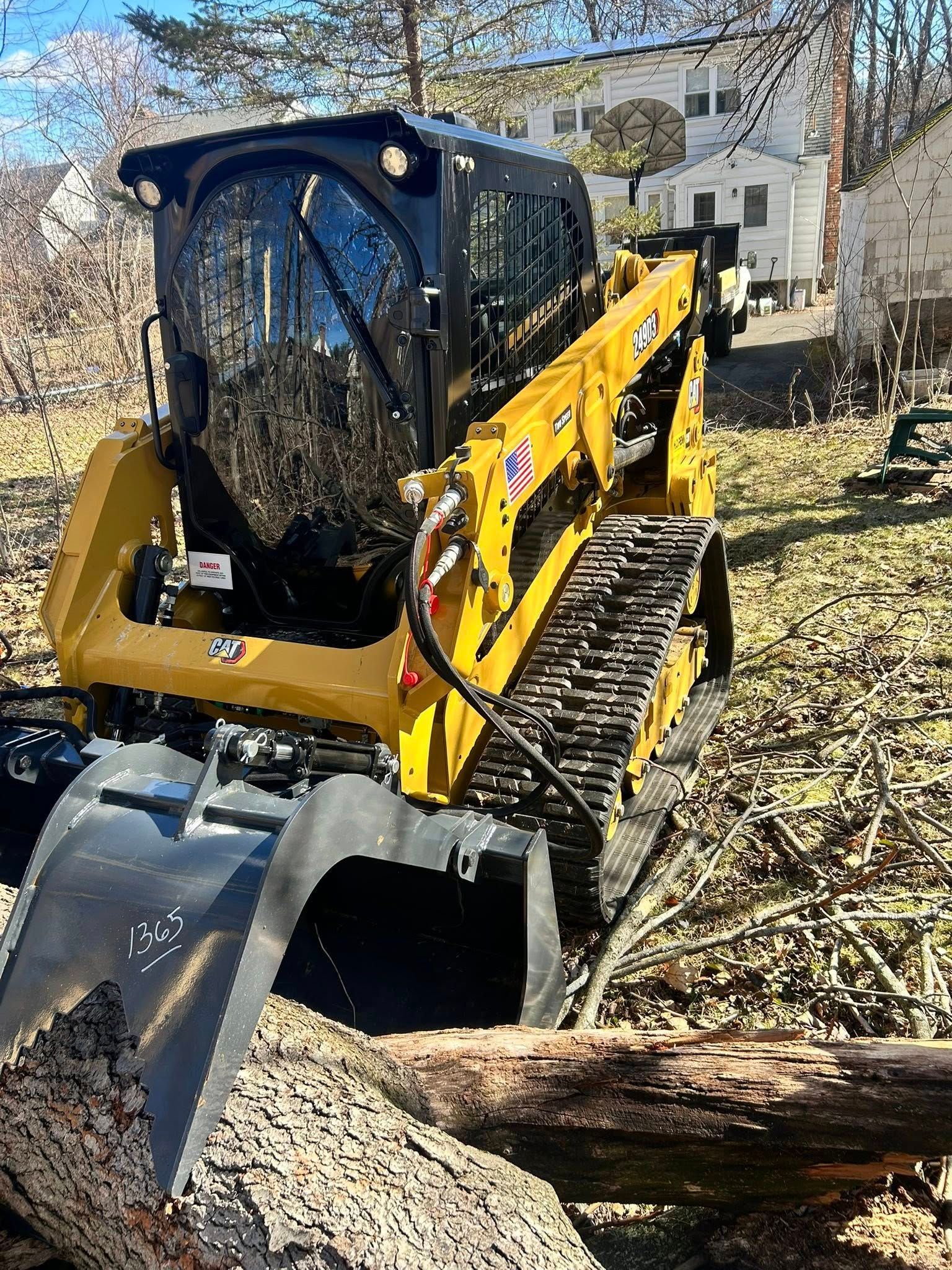 Yellow compact excavator clearing a fallen tree branch in a yard