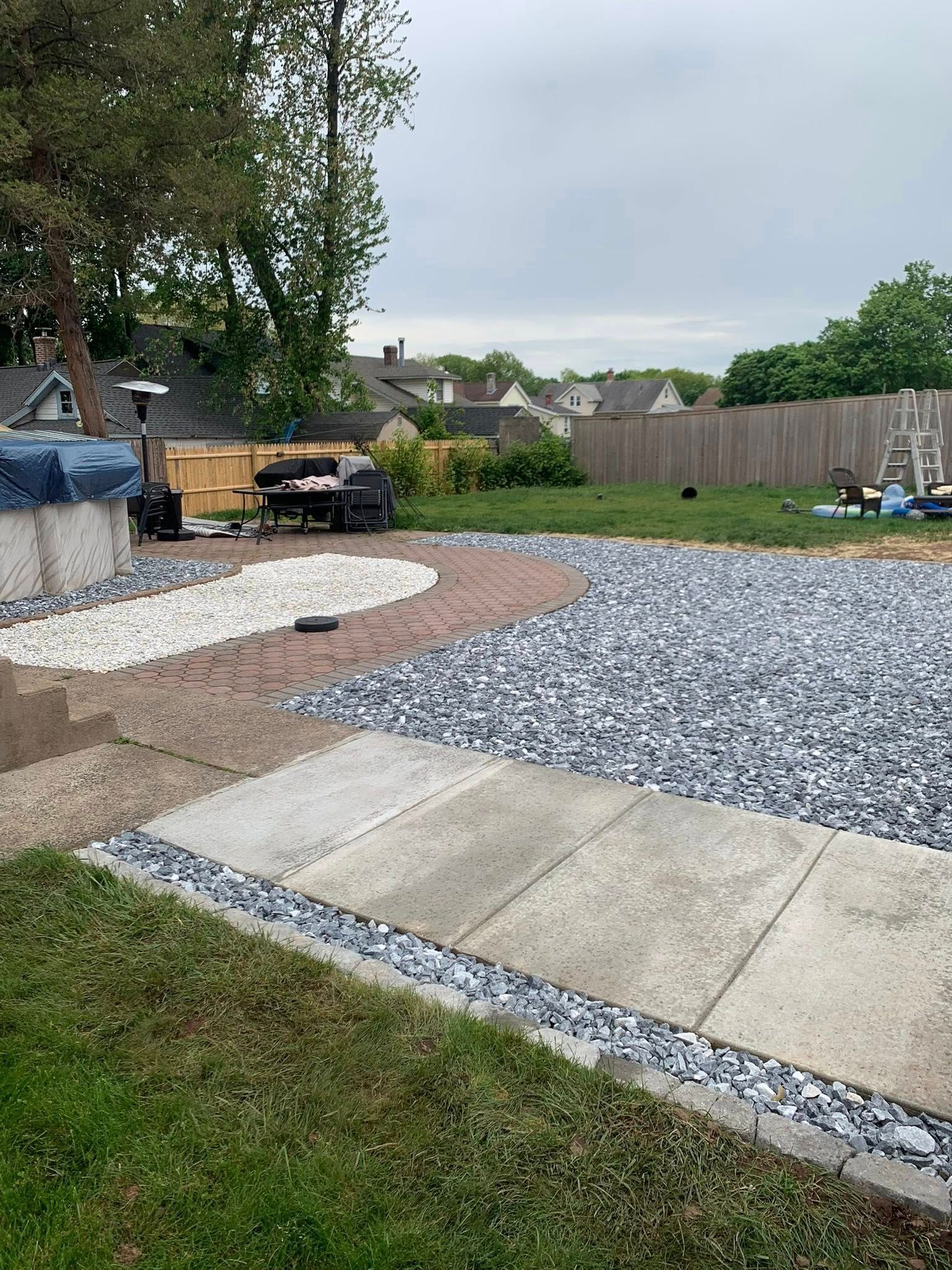 Backyard with gravel and concrete patio, grass lawn, and wooden fence under cloudy sky