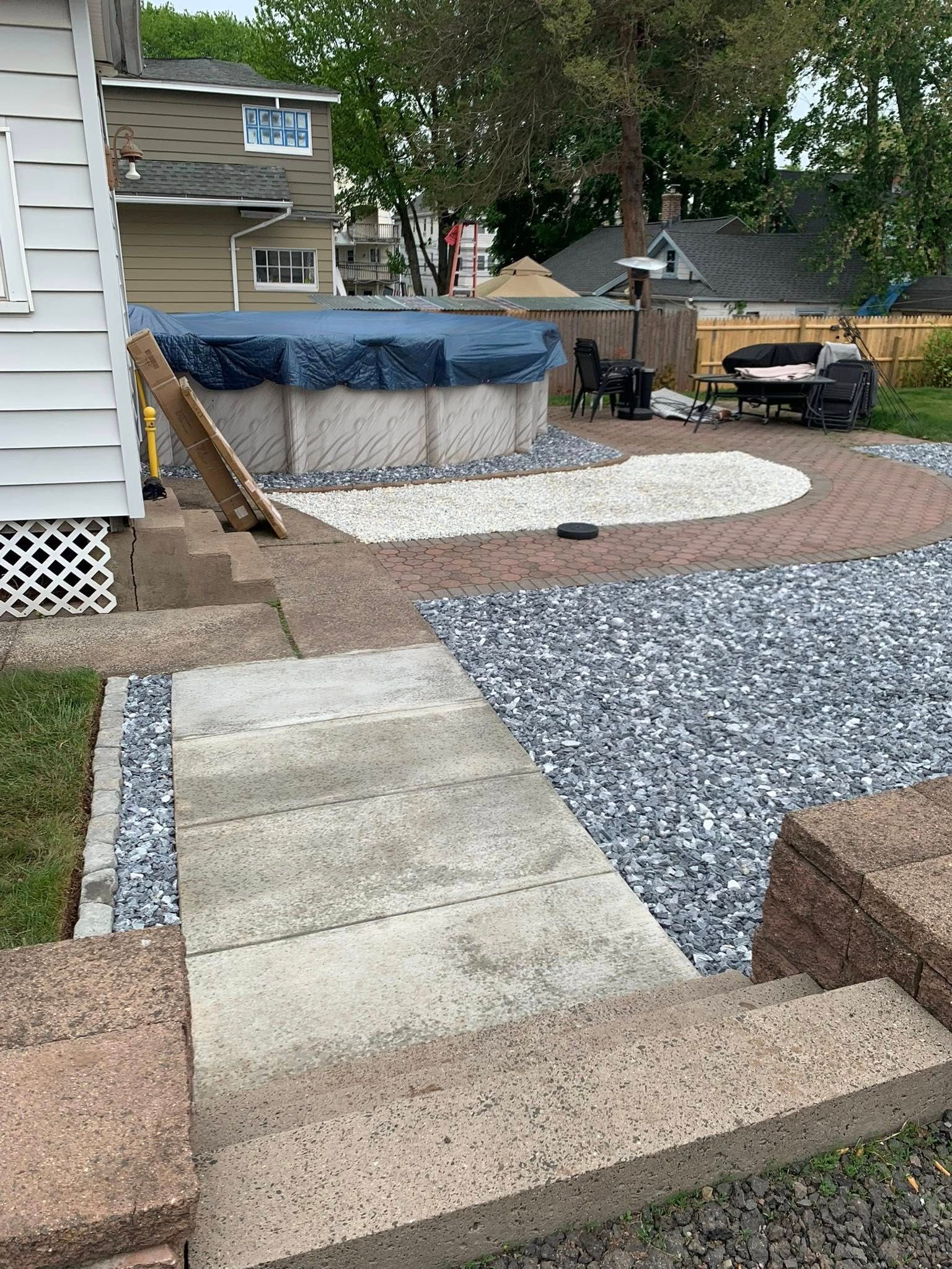 Backyard patio with stone steps, gravel paths, and an above-ground pool beside a house.