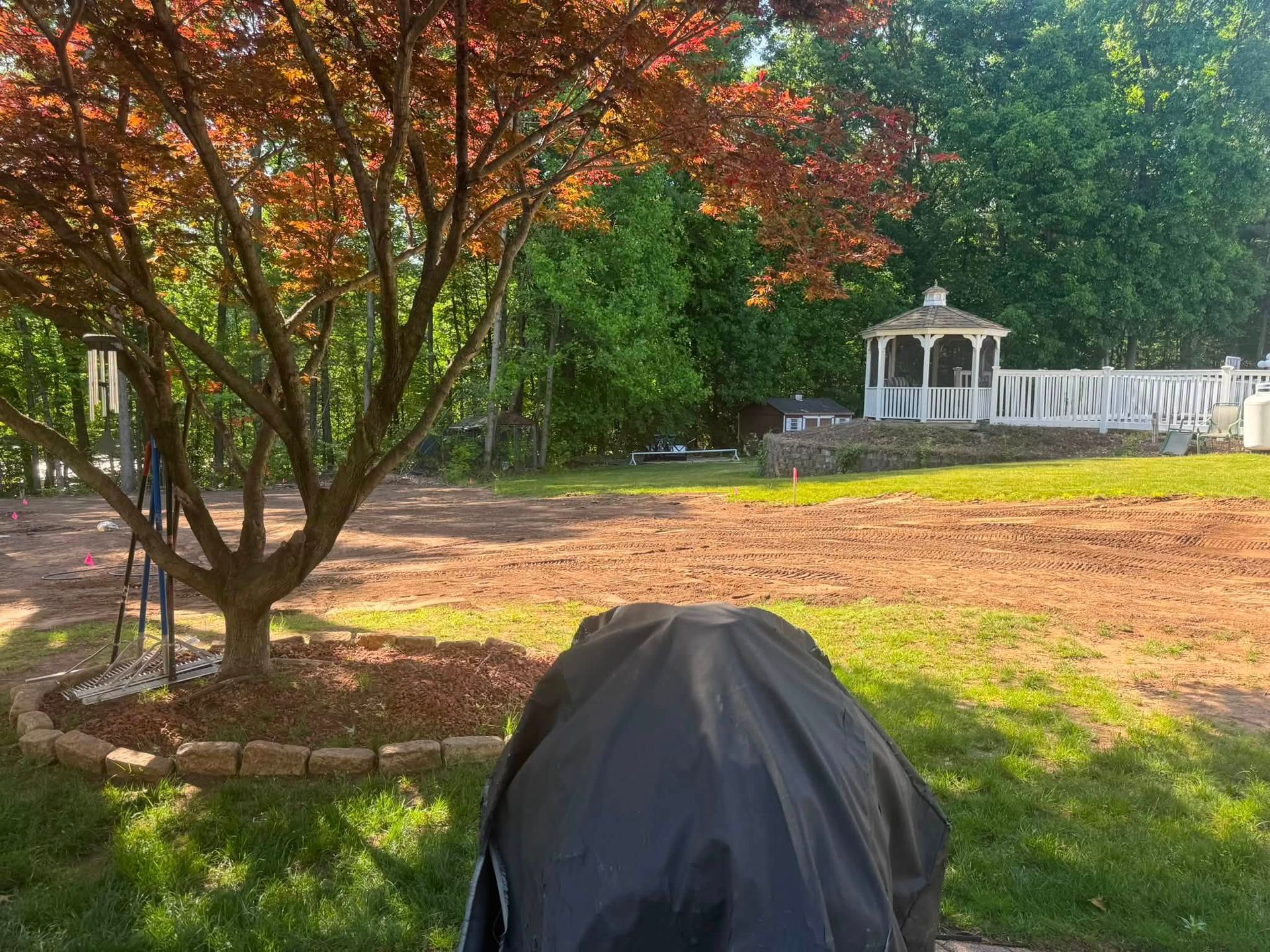 Backyard with a leafy tree, black grill cover, and white gazebo on a sunny day
