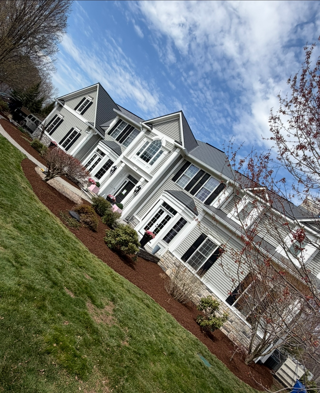 White suburban houses with gray roofs and white columns along a grassy lawn under a blue sky