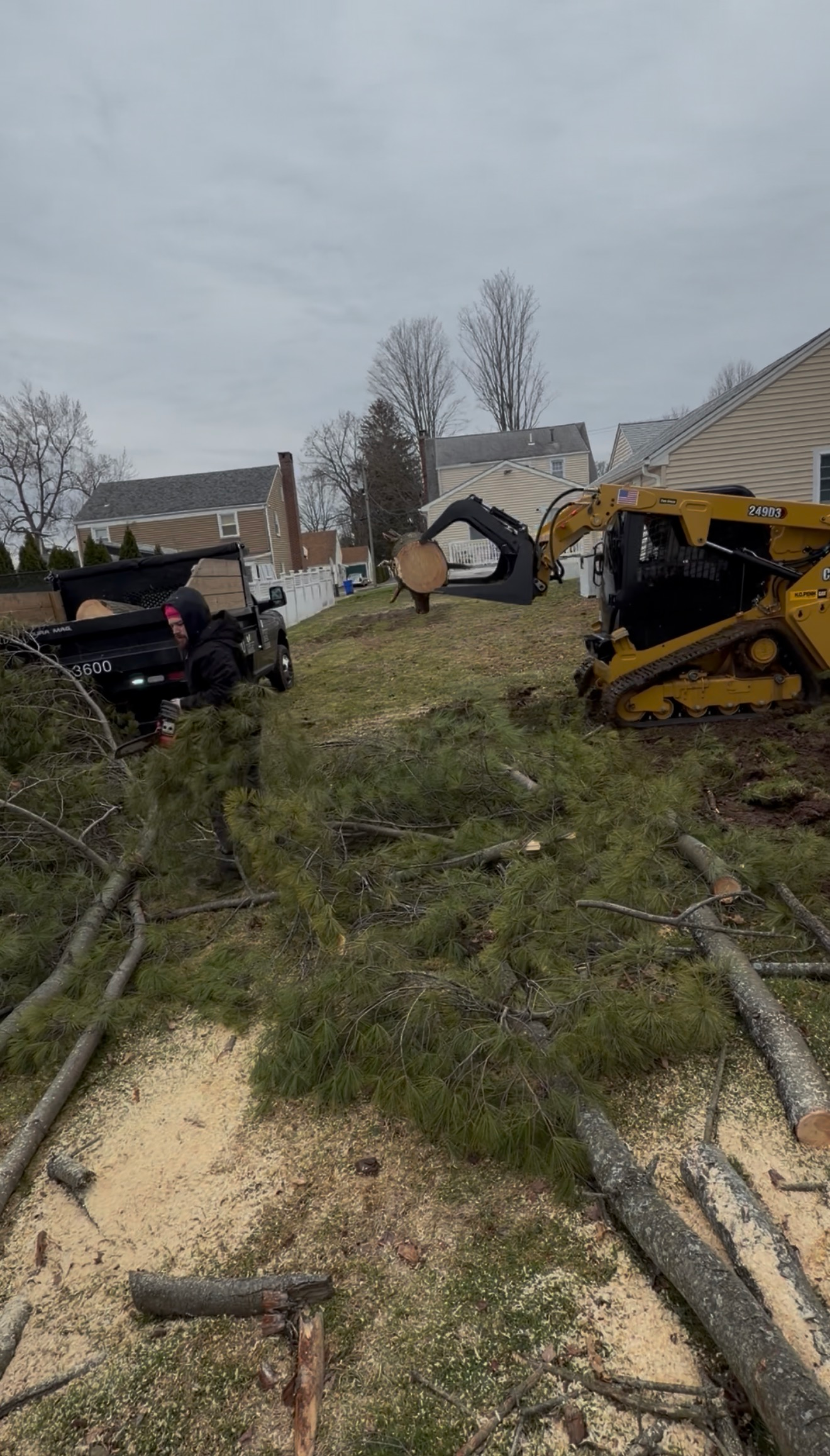 Damaged utility trucks and debris in a grassy area beside a flooded path under a gray sky