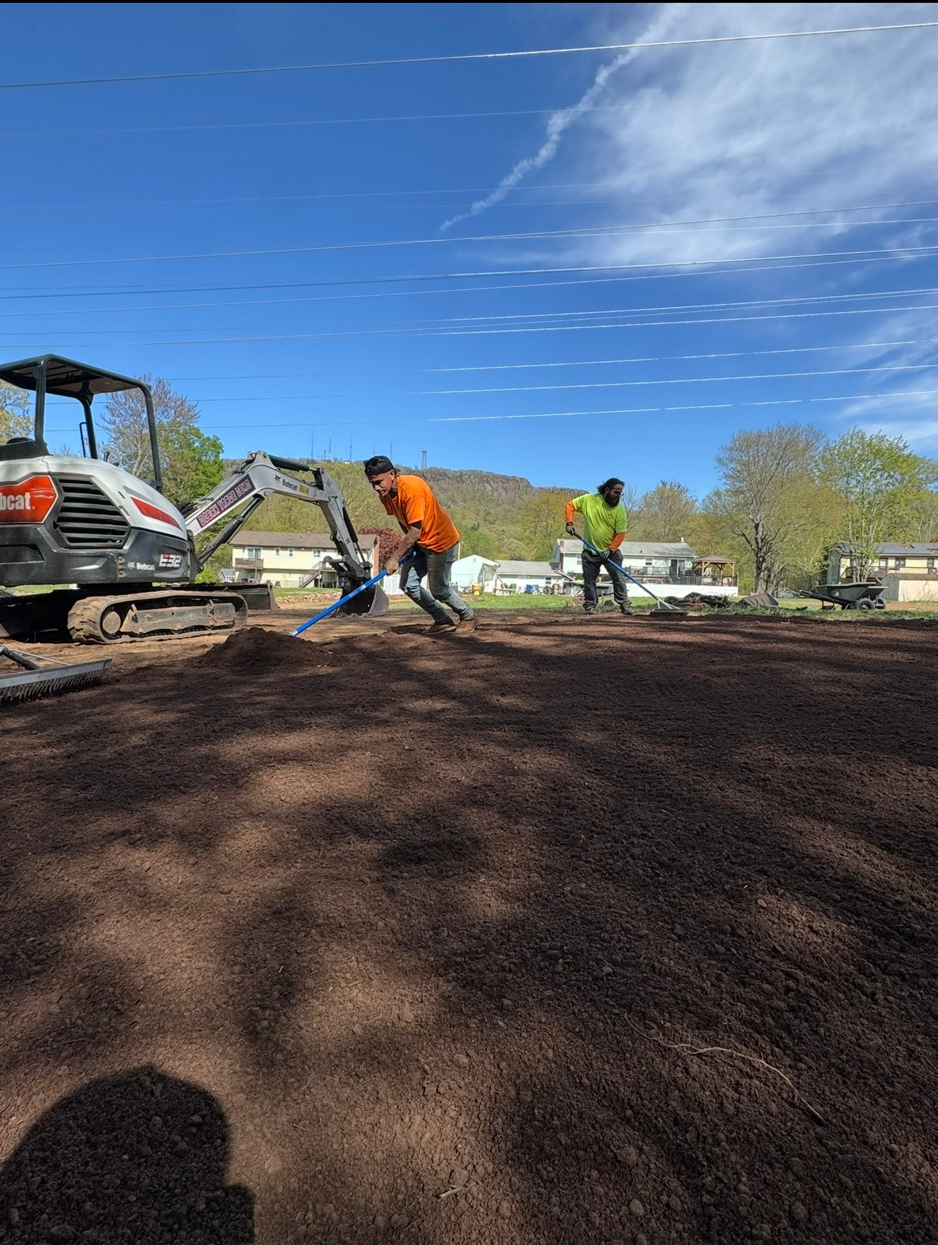Workers paving a driveway beside an excavator under a bright blue sky