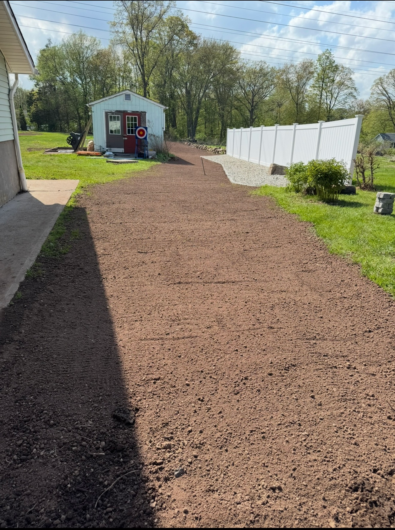 Fresh mulch path leads to a small shed in a backyard, with grass and a white fence on the right.