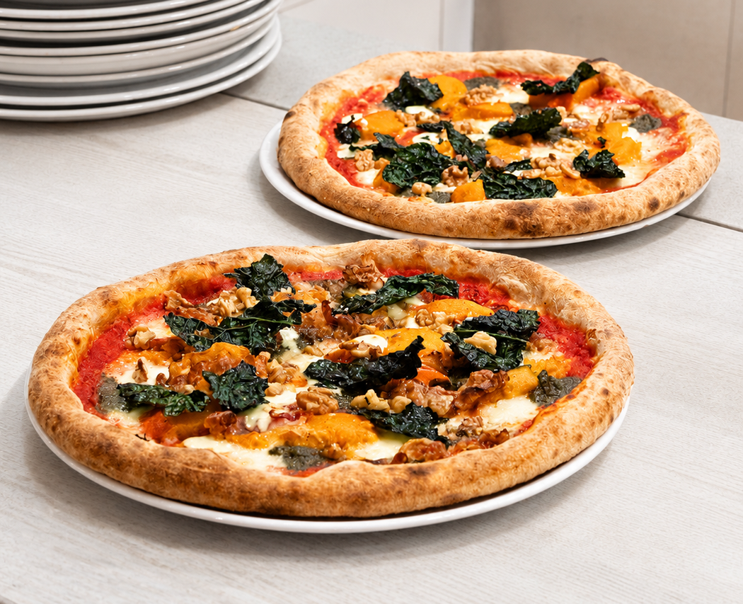 Due pizze con verdure a foglia verde e pomodori su piatti bianchi su un bancone