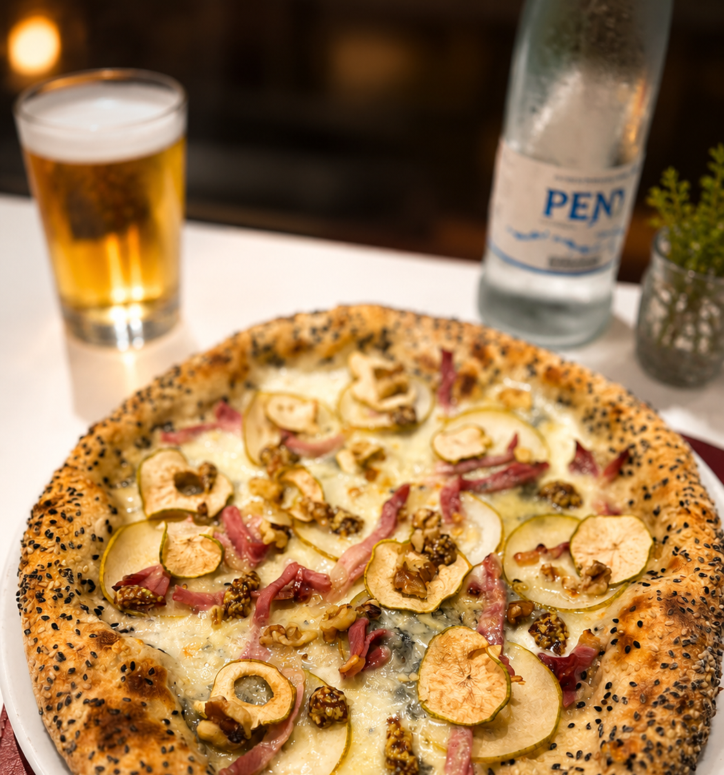 Una pizza con patate, pancetta e cipolla rossa su un tavolo, accanto a un bicchiere di birra e una bottiglia d'acqua.