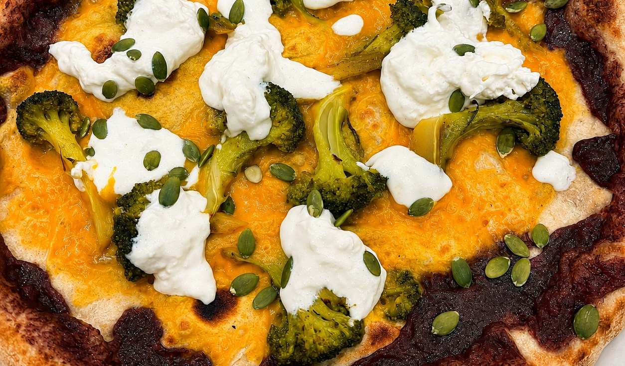 Focaccia al formaggio guarnita con ciuffi bianchi ed erbe aromatiche, con crosta bruciacchiata e salsa all'arancia sul fondo.