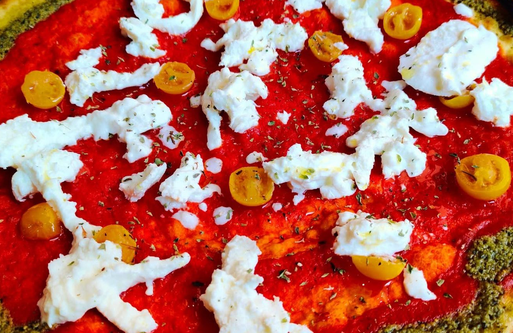 Primo piano di un impasto per pizza rosso guarnito con formaggio bianco e fette di peperone giallo.