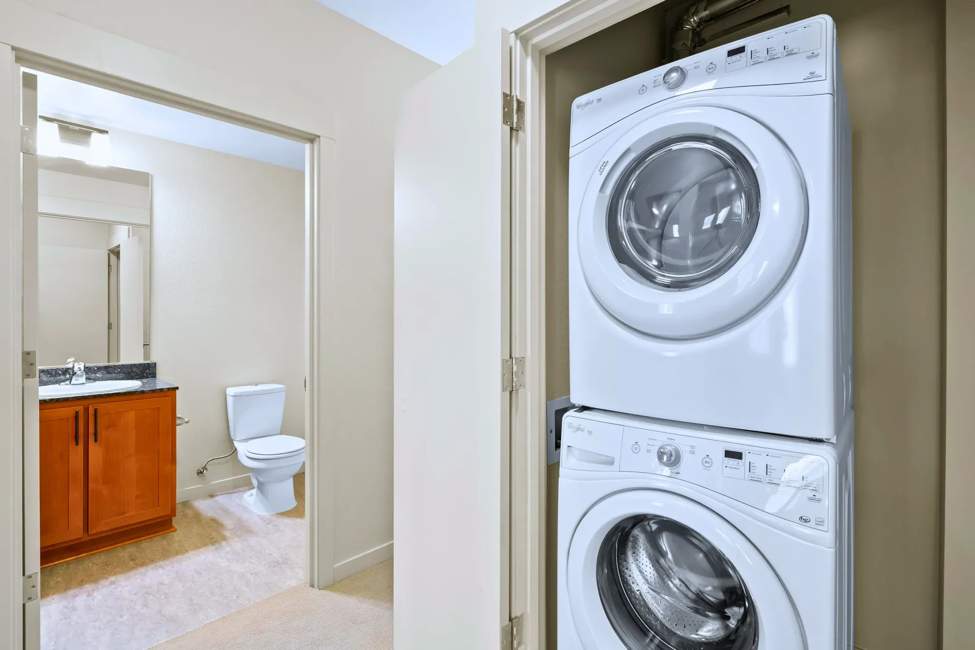 Stacked washer and dryer in a laundry closet beside a bathroom vanity.