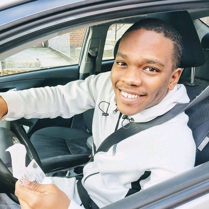 A man in a white sweatshirt is smiling while driving a car