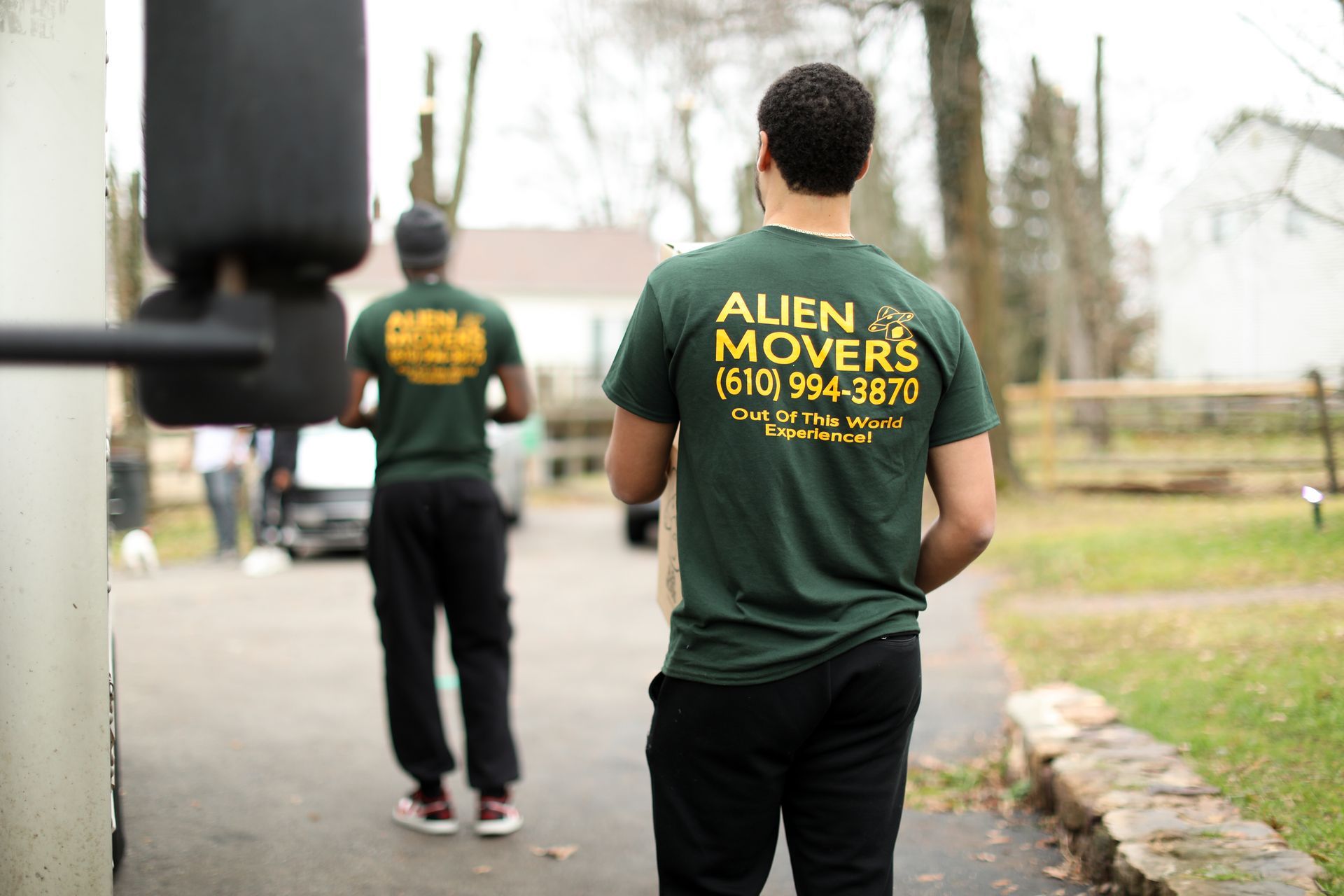 A mover from Alien Movers stands thoughtfully in a stylish grey-toned hallway, with a chair and toolbox ready for home relocation tasks, reflecting the company's detail-oriented moving services.
