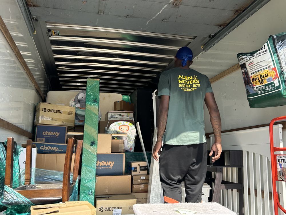 A mover from Alien Movers, identifiable by the company logo on the back of his shirt, carefully assessing the packed items in a moving truck, ensuring a secure and orderly move for a Philadelphia client.
