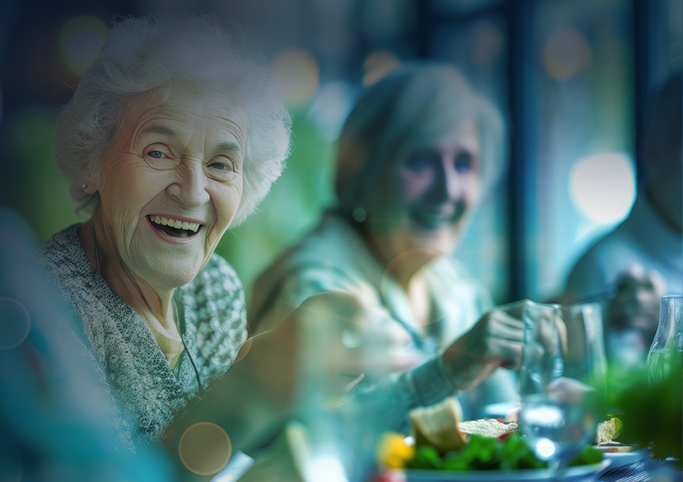 Elderly woman smiling at a table, enjoying a meal with others.