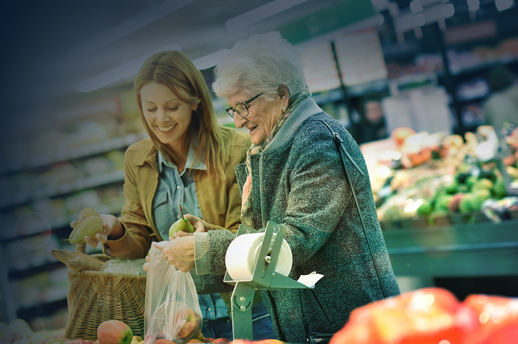 Woman helps an older person select produce in a grocery store.