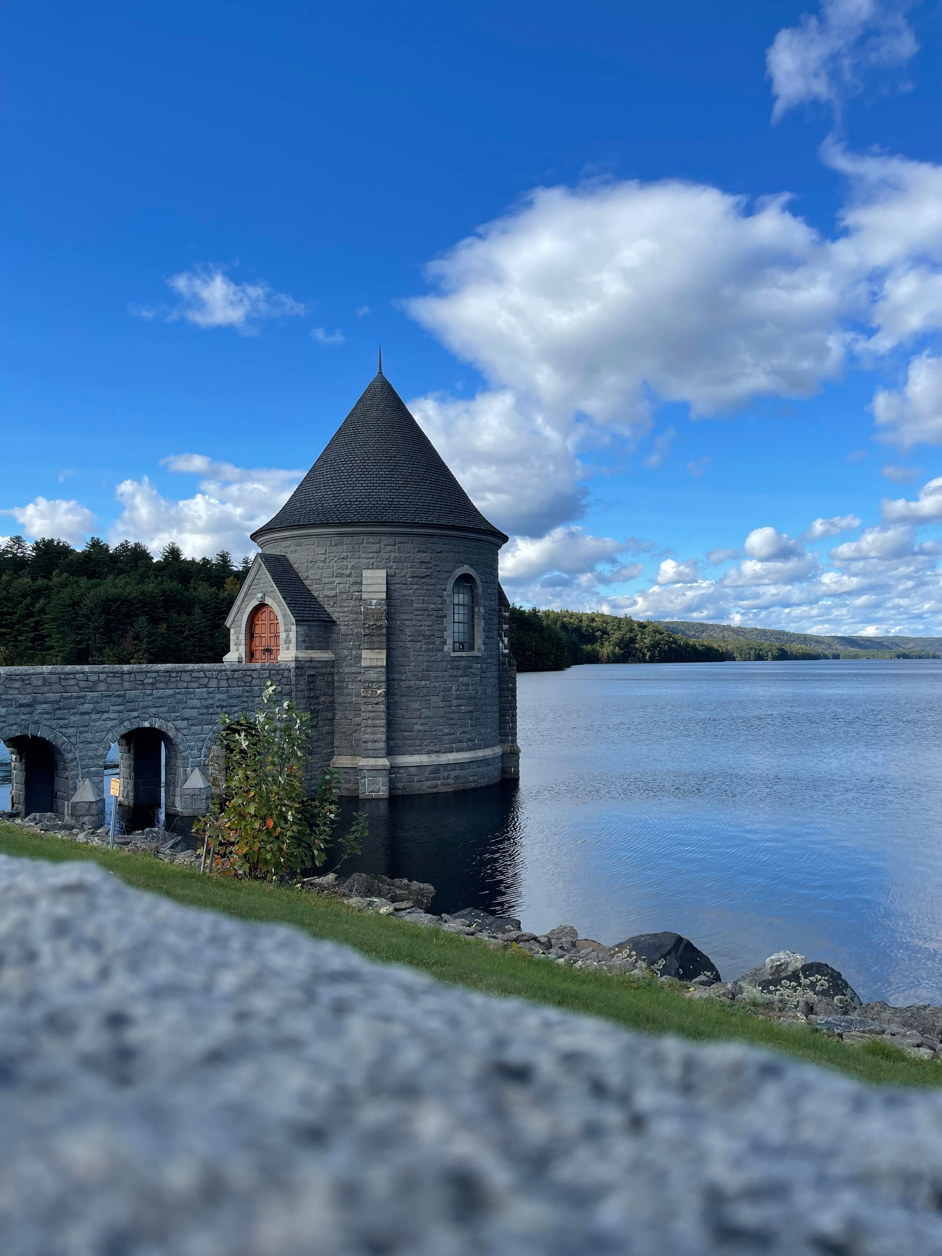 Stone tower on a dam, overlooking a lake under a blue sky with clouds.