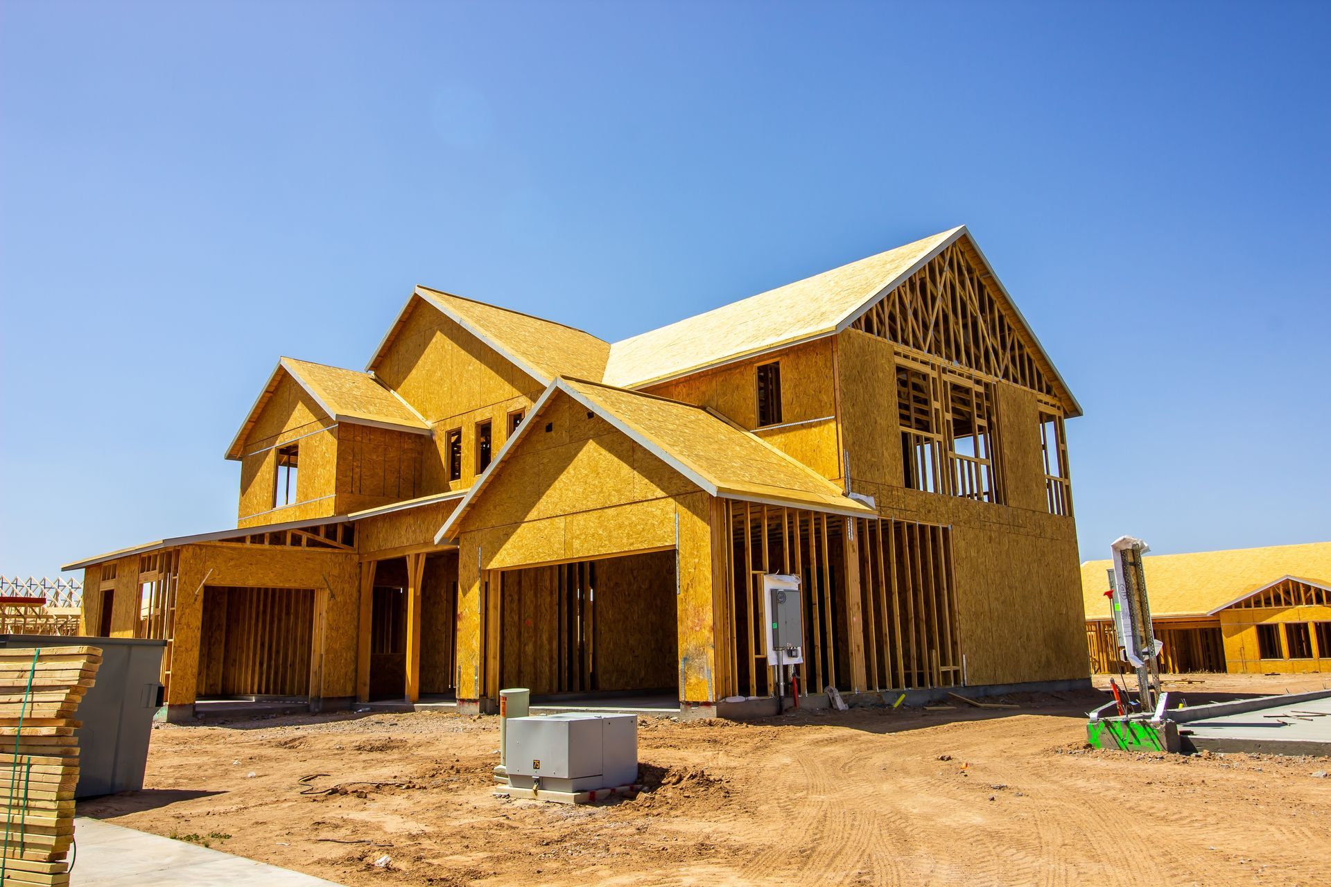Two-story house under construction, framed with exposed wooden beams, on a dry, sunny day.