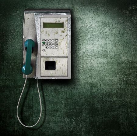 Vintage wall-mounted payphone with a teal handset on a textured green wall.