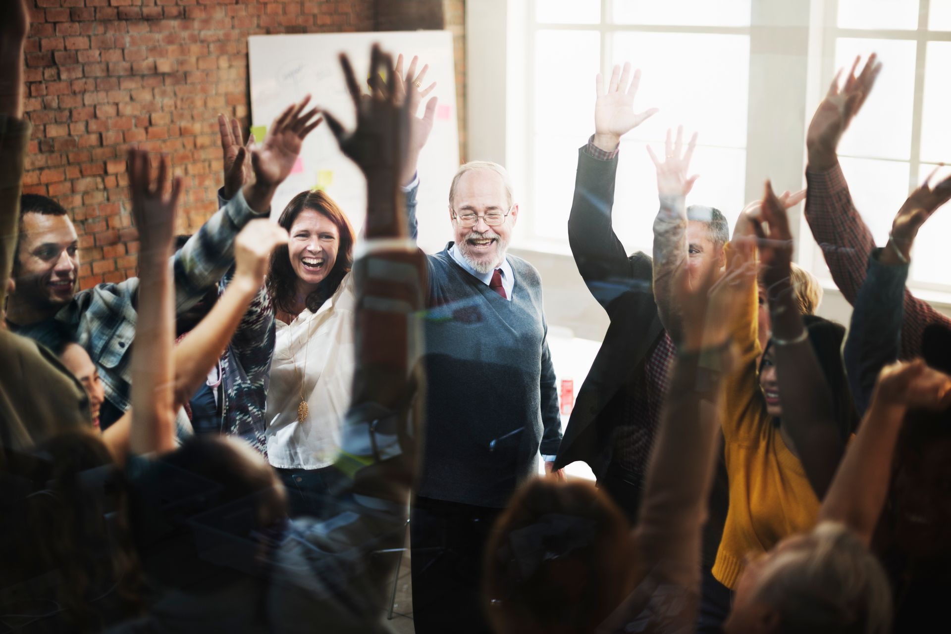People indoors celebrating with raised hands and smiles in a bright room with brick wall and windows