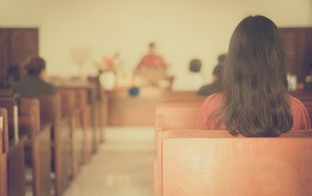 Person sitting in a church pew facing the altar in a softly lit sanctuary