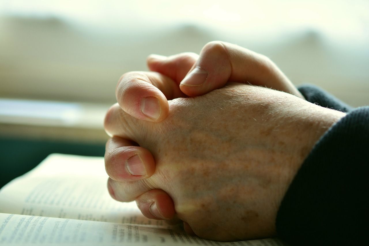 Clasped hands resting on an open book in soft daylight
