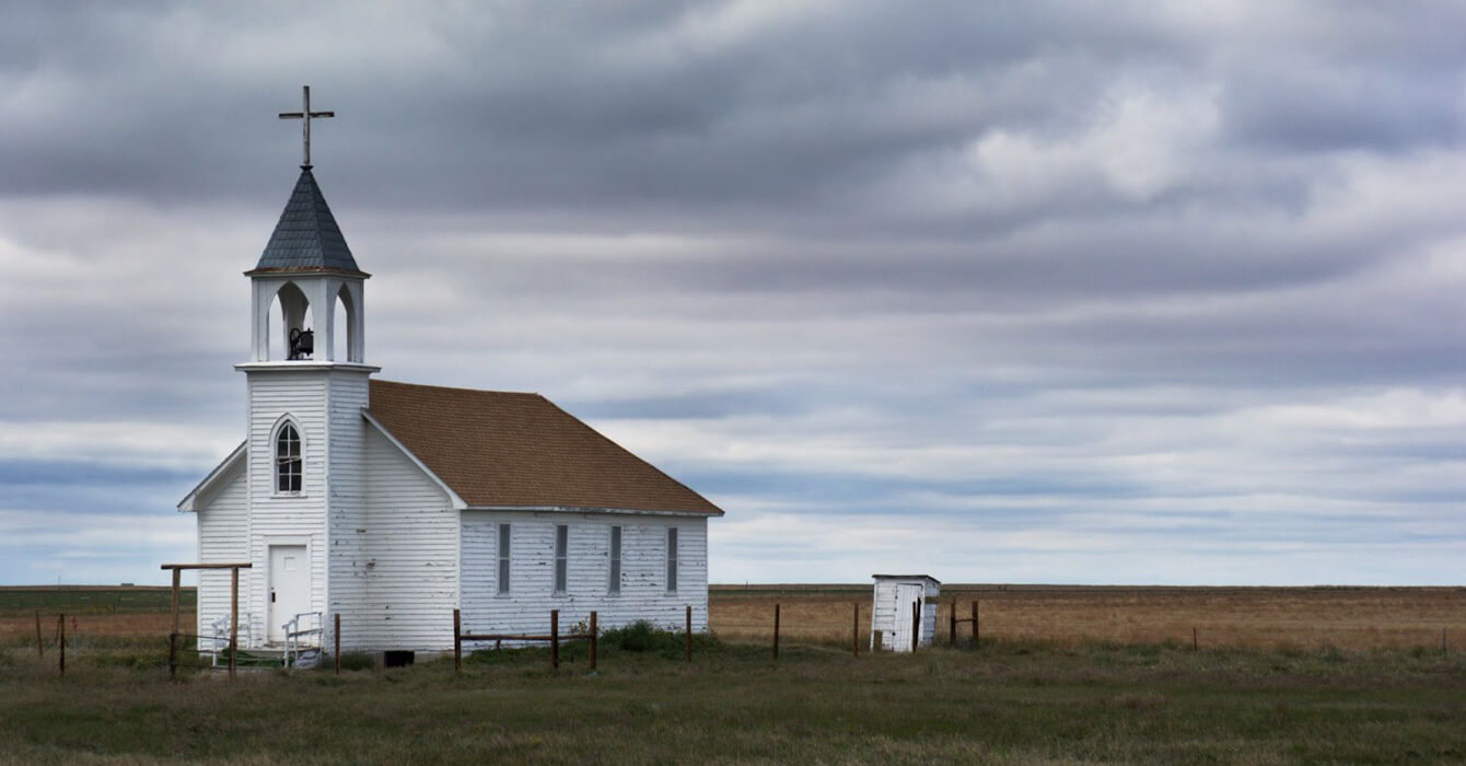 Small white church with a steeple in a flat, cloudy rural landscape