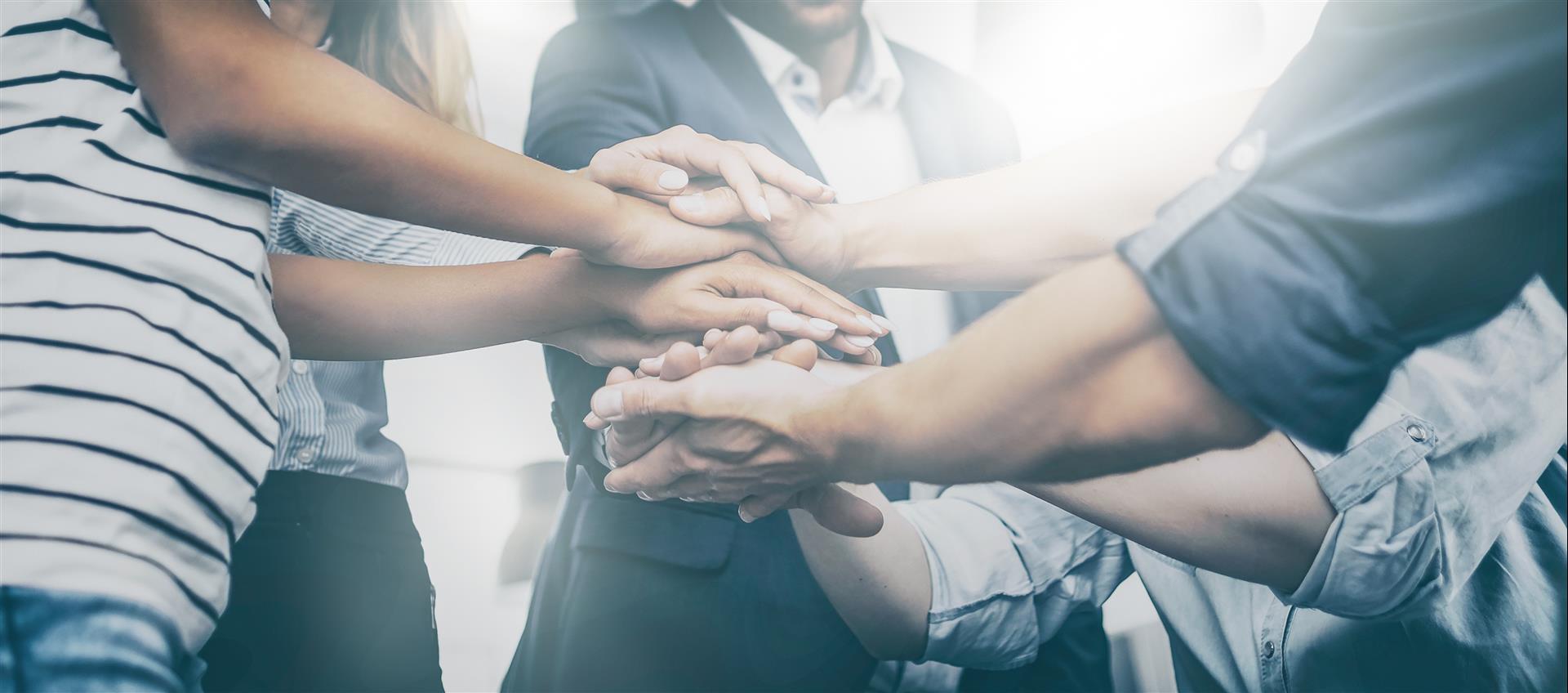 Hands stacked together in a team huddle, with bright light in the background.