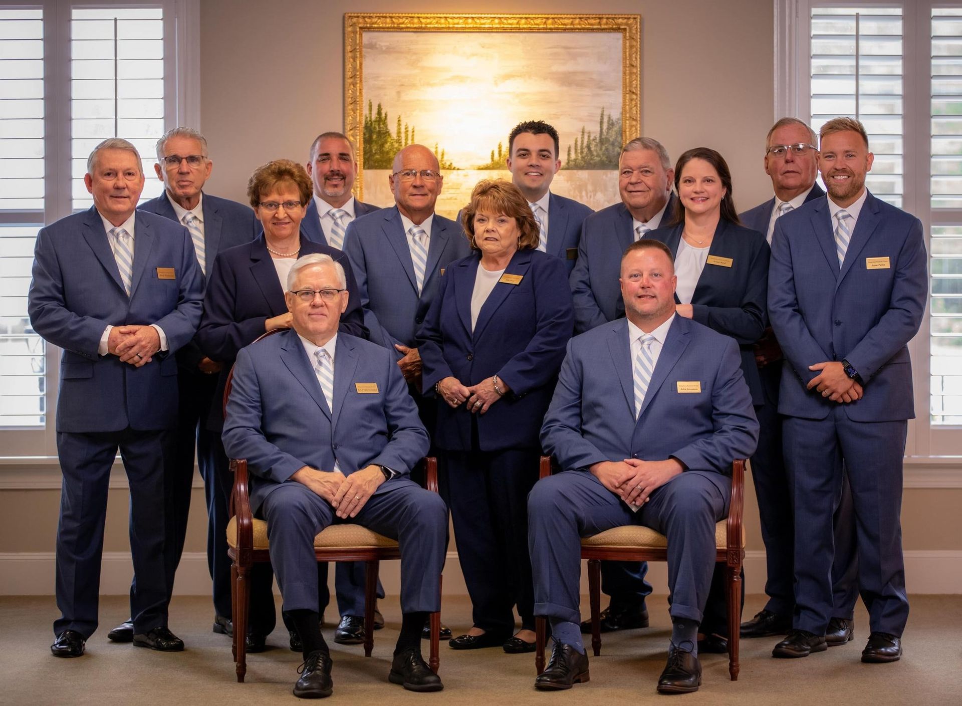 A group of professionals in suits posing for a formal portrait in front of a landscape painting.