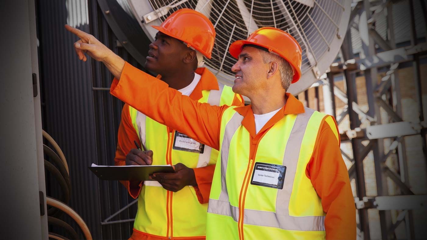 Dos trabajadores de la construcción que llevan cascos y chalecos de seguridad miran una tableta.